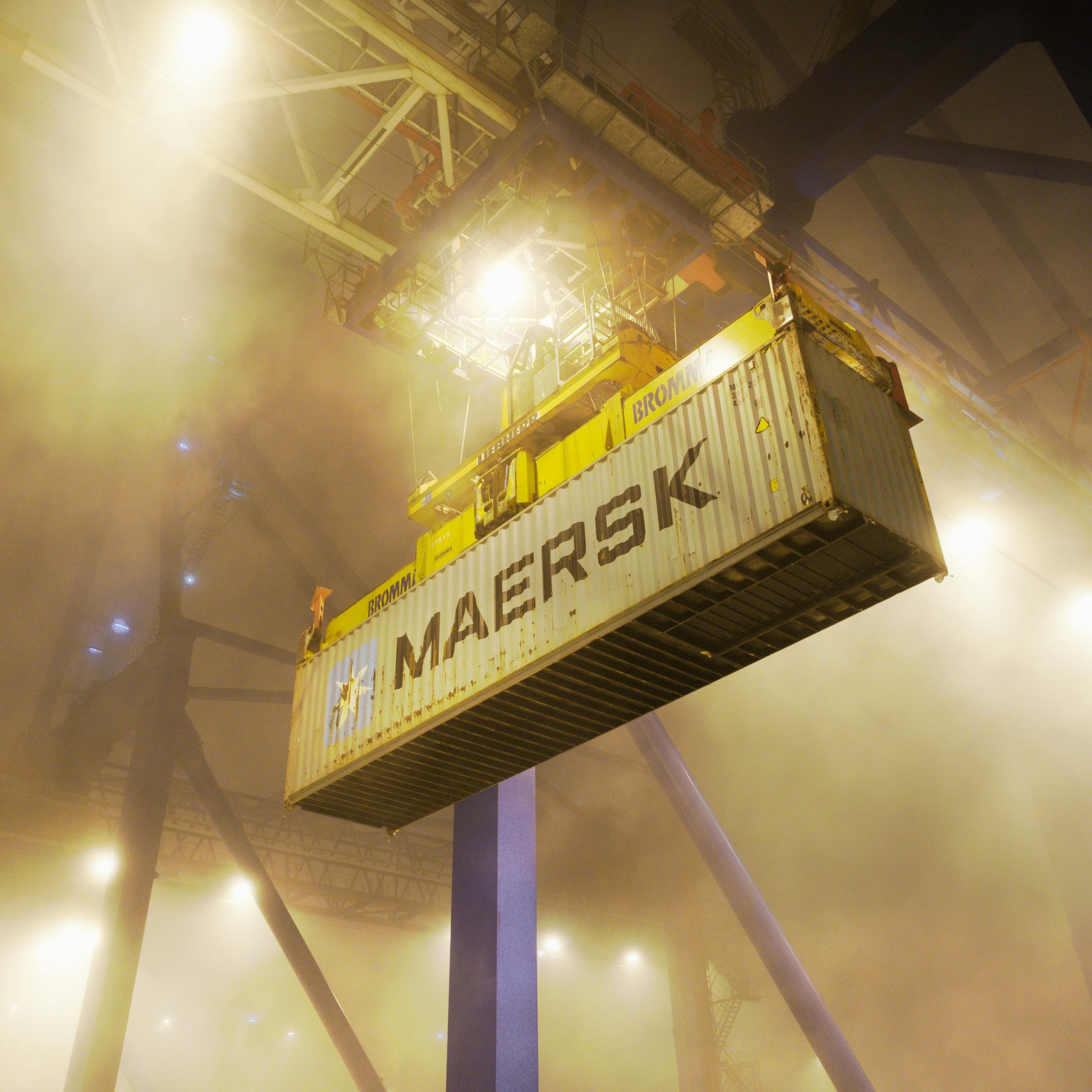 Industrial shipping container suspended by crane in Gdańsk port at night.